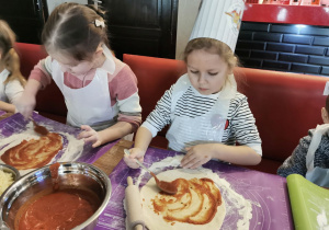 Ala i Gabrysia smarują swoje ciasta sosem pomidorowym.