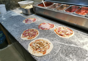 Przygotowane pizze leżą na blacie i czekają na włożenie do pieca.
