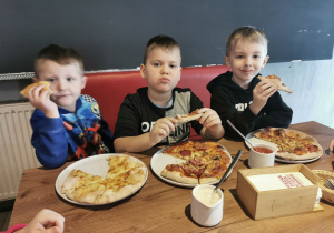 Tomek, Hubert i Oliwier z apetytem zjadają swoje pizzę.