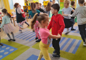 Dziewczynki tańczą w parach z chłopcami na dywanie.