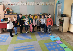 Dzieci z grupy "Słoneczek" ustawione na dywanie czekają na rozpoczęcie pokonywania matematycznego toru przeszkód.