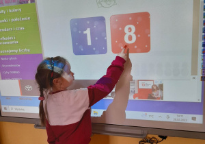 Alicja podczas gry "Która liczba jest większa?" wskazuje na tablicy multimedialnej większą liczbę - osiem.