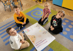 Winicjusz, Hubert, Natalia i Hubert siedzą na dywanie wokół plakatu przedstawiającego różne rodzaje dymów.