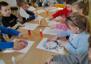 Dzieci naklejają pokolorowane znaki na sztywny karton w kolorze białym.