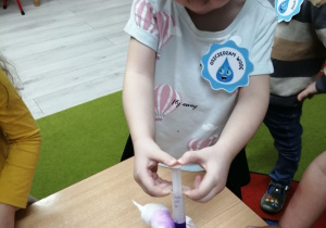 Emma zabarwia piankę do golenia w kubeczku fioletową wodą znajdującą się w plastikowej strzykawce.