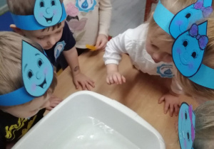 Dzieci stoją i obserwują przedmioty wrzucone do miski z wodą czy utoną czy będą pływały.
