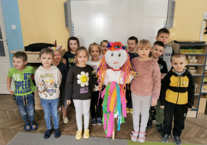 Dzieci z grupy "Słoneczka" stoją przed tablicą multimedialną i z uśmiechami na twarzach prezentują wykonaną Marzannę