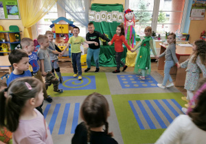 Dzieci z grupy "Słoneczka" w trakcie zabawy ruchowej przy piosence tańczą na dywanie trzymając się za ręce.