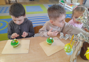 Gabrysia, Oskar i Igor siedzą obok siebie i dekorują muffinki.
