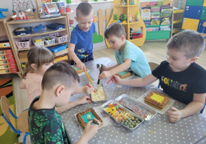 Dzieci z grupy "Biedronek" siedzą przy stole i ozdabiają świąteczne mazurki kolorowymi lukrami i posypkami