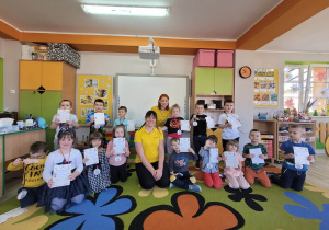 Wspólne zdjęcie dzieci z grupy "Biedronek" i pracownic cukierni Ozdowscy. Przedszkolaki trzymają w dłoniach dyplomy, a na szyjach mają zawieszone ciasteczkowe medale .