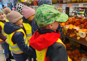 Dzieci oglądają w sklepie owoce w skrzynkach.