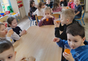 Dzieci siedzą przy stołach i z apetytem piją zakupione soki "Kubuś".