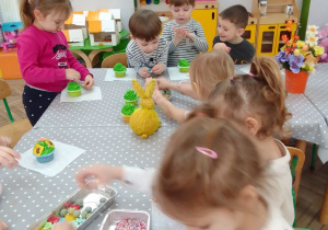 Dzieci ozdabiają cukrowymi dekoracjami babeczki pokryte zielonym kremem.