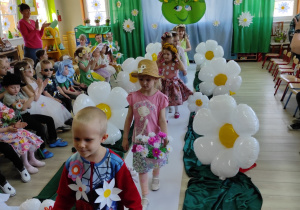 Dzieci prezentują swoje kwiatowe stroje na wybiegu, wzdłuż wybiegu – balony w kształcie stokrotek, z tyłu dekoracja: na niebieskim tle zielona buzia ze stokrotkami, na górze napis – Dzień Ziemi.