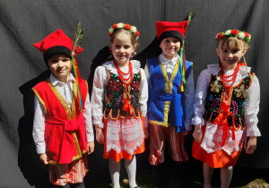 Oskar, Alicja, Krzyś i Oliwia ubrani w stroje krakowskie stoją przy scenie w parku Traugutta.