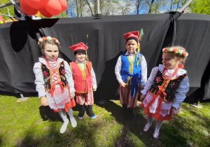 Wiktoria, Bruno, Hubert i Natalia stoją przy scenie w parku Traugutta. Dzieci w strojach krakowskich czekają na występ.