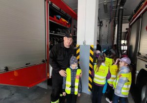 Dzieci oglądają wóz strażacki w garażu, a Igor pozuje do zdjęcia razem ze strażakiem - tatą Krzysia.