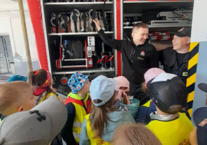 Strażacy prezentują dzieciom węże w wozie strażackim.