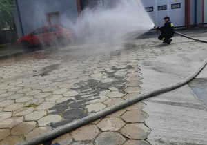 Strażak przedstawia pokaz lania wody z węża strażackiego podczas gaszenia pożaru.
