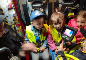 Antek, Wiktoria i Lena w wozie strażackim oglądają kamerę termowizyjną, którą prezentuje jeden ze strażaków.