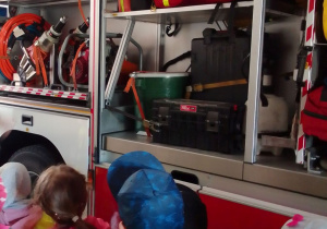 Dzieci obserwują wyposażenie wozu strażackiego.