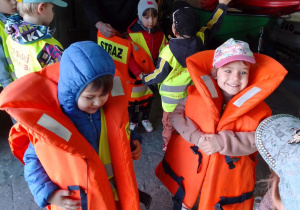Grupa dzieci prezentuje na sobie kamizelki asekuracyjne w kolorze pomarańczowym.
