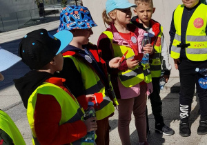 Dzieci stoją obok siebie podczas rozwiązywania zadania i trzymają w rękach karteczki. Krzyś czyta pytanie dotyczące naszego miasta.