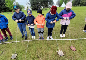 Grupka dzieci nawija na patyczek sznurek przyczepiony do drewnianego żółwia podczas konkurencji - "Wyścigi żółwi".