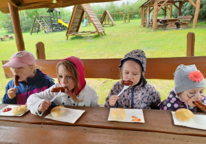 Czworo dzieci siedzi przy stole i degustuje upieczone kiełbaski.