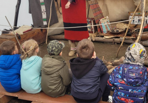 Dzieci siedzą na ławeczce wewnątrz indiańskiego namioty - tipi. Przedszkolaki słuchają o tradycjach i kulturze Indian.
