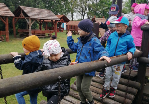 Dzieci podczas zabawy na placu zabaw przechodzą przez ruchomy mostek.
