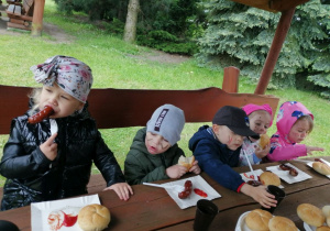 Grupka dzieci siedzi przy stole podczas degustowania kiełbasek.
