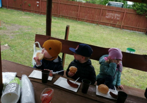 Grupka dzieci siedzi przy drewnianym stole podczas degustowania kiełbasek.