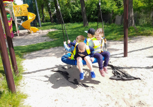Czworo dzieci podczas zabawy na placu zabaw siedzi w gnieździe bocianim.