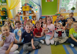Dzieci siedzą w sali przedszkolnej i prezentują otrzymane od mamy Alicji drewniane zakładki, które pięknie ozdobiły.