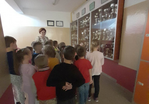 Dzieci stoją w korytarzu i oglądają puchary umieszczone w gablocie na ścianie.