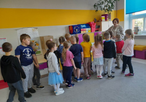 Dzieci oglądają kolejną salę lekcyjną. Pani nauczycielka pokazuje przedszkolakom szafki z pomocami.