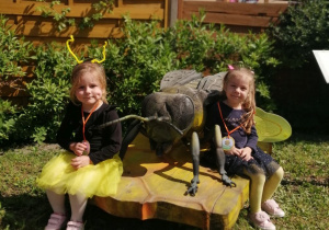 Dwie dziewczynki siedzą przy rzeźbie pszczoły.