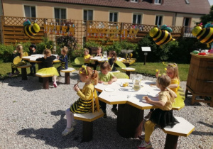 "Pszczółki" przy stolikach degustują miód na wafelkach.