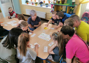 Dzieci wspólnie z rodzicami siedzą przy stołach podczas zabawy "Zakodowane działania".