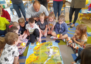 Grupka dzieci siedzi wokół maty "Mapa skarbów". Krzyś razem z tatą programuje trasę Bee Bota do celu.