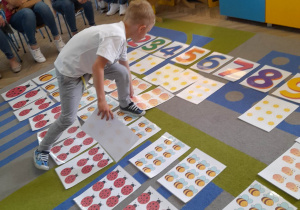 Na dywanie leżą ułożone przez dzieci karty z różną liczbą elementów i karty z cyframi. Hubert po przeliczeniu elementów dokłada kartę w okreslone miejsce.