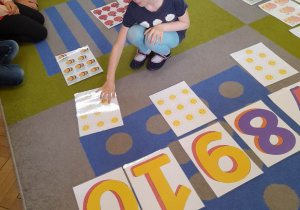 Amelia podczas gry "Wiosenne kodowanie" przykucnęła na dywanie i liczy słoneczka na wybranej przez siebie karcie.