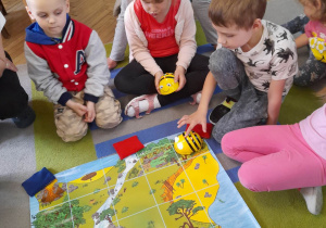 Grupka dzieci siedzi na dywanie przed matą "Mapa skarbów". Hubert programuje Bee Bota. Obok chłopca siedzi Alicja z mamą. Dziewczynka trzyma drugą pszczółkę w ręku.