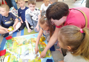 Grupka dzieci siedzi wokół maty "Mapa skarbów". Alicja wspólnie z mamą wyznacza trasę Bee Bota co celu.
