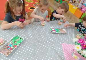 Dzieci ozdabiają cukrowymi dekoracjami babeczki pokryte różowym kremem.