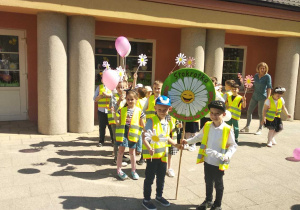 Grupa "Biedronek" z balonami, stokrotkami i z tablicą z logo przedszkola pozuje do pamiątkowego zdjęcia.
