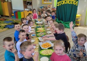 Dzieci z grupy Biedronek siedzą przy stoliku w sali przedszkolnej. Na stoliku widać smakołyki przygotowane dla dzieci