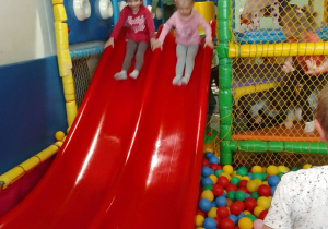 Wiktoria i Łucja zjeżdżają na czerwonej zjeżdżalni do basenu z kolorowymi piłeczkami.
